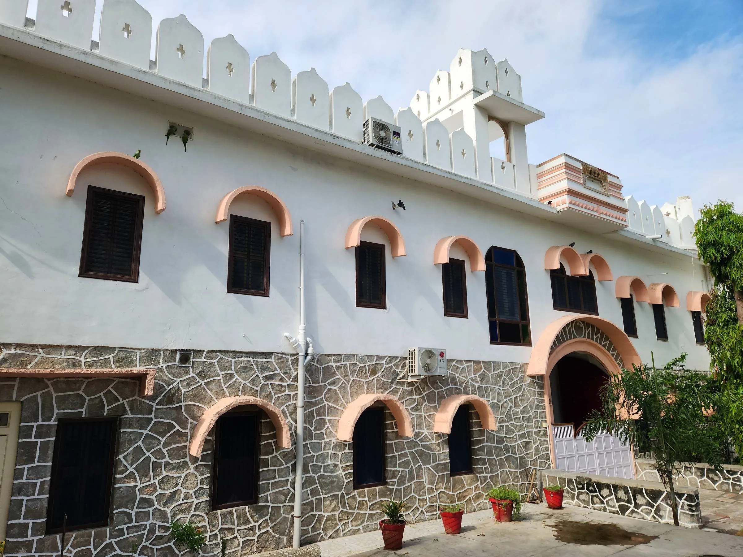 The arcade along the courtyard at Rawla Bankli — a run of pink-trimmed arches over rough stone, terracotta pots ranged along the wall