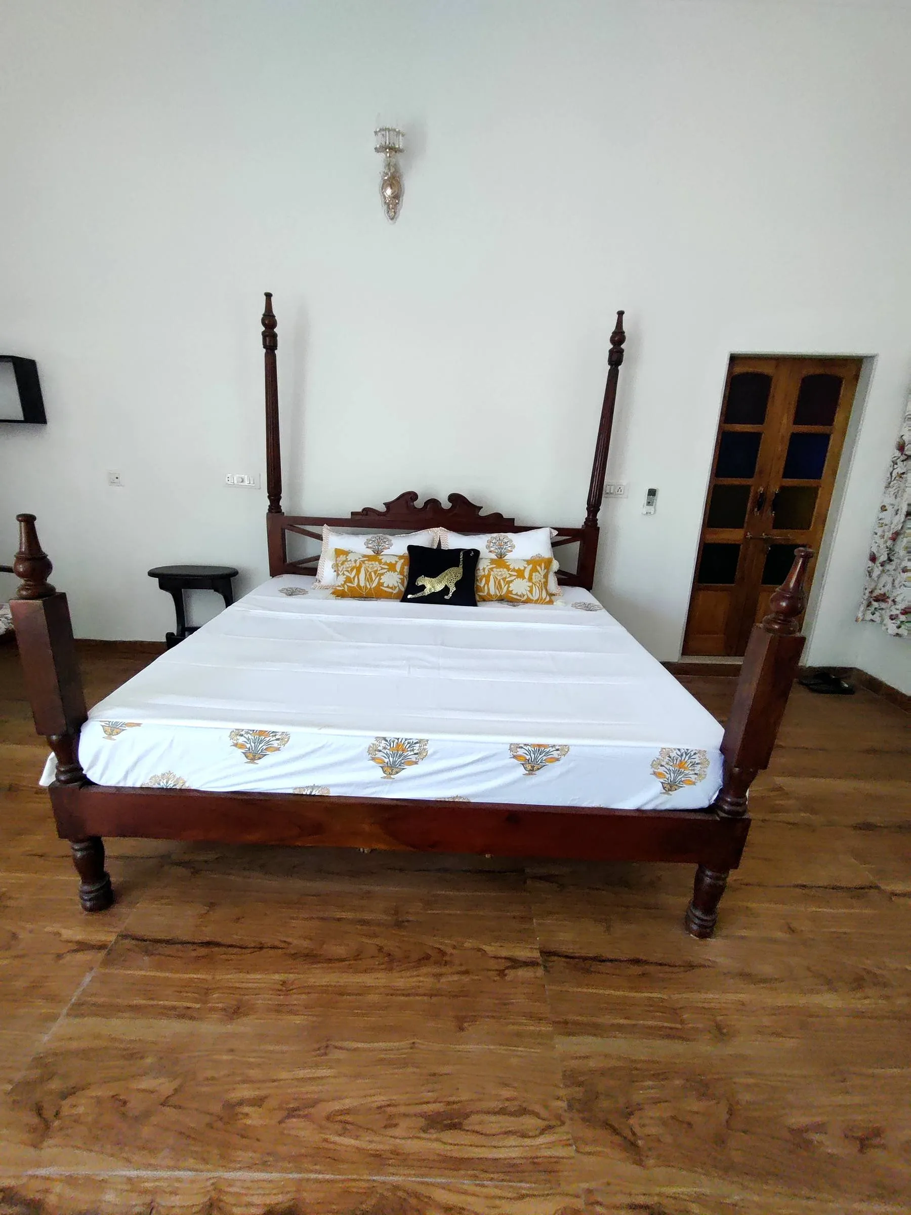 A carved wooden four-poster bed dressed in white linen, seen straight on across a wide-plank floor
