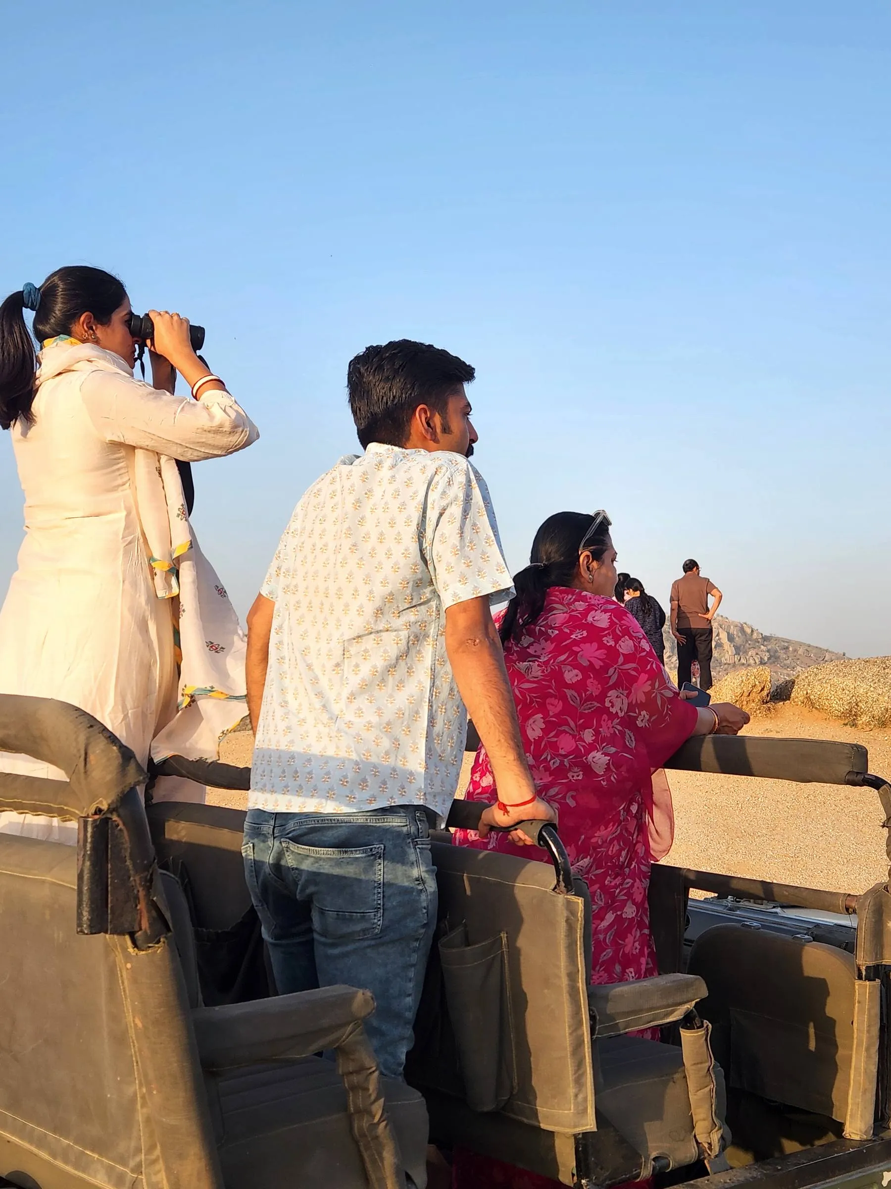 Guests standing in an open jeep at sunrise, watching the hillside through binoculars