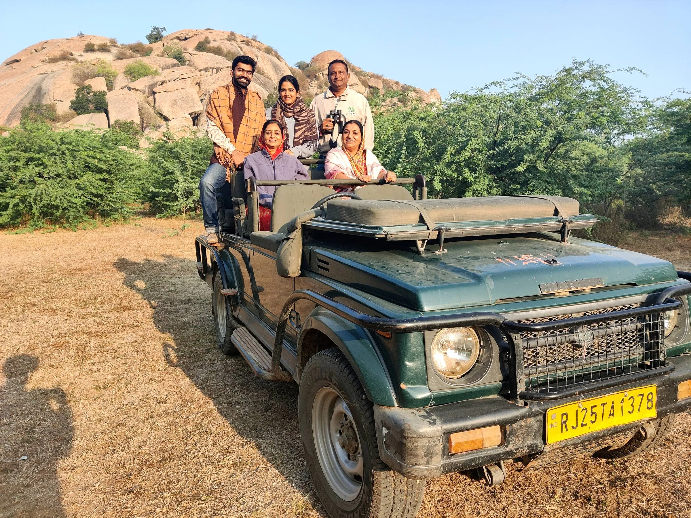 Guests seated in an open safari jeep at the foot of a granite hill, ready for the morning drive