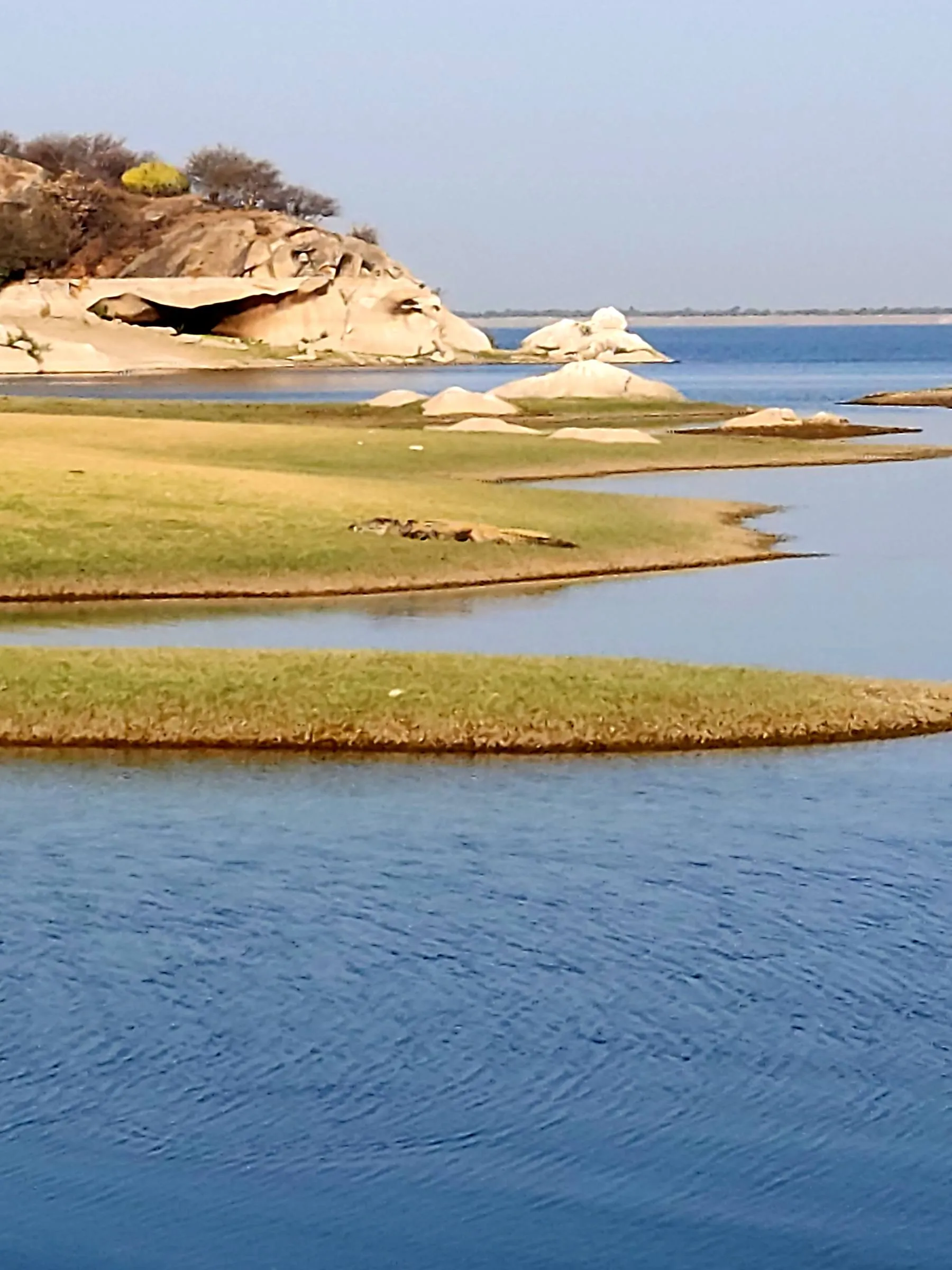 Wide open water at Jawai Dam, broken by low grass islands and pale granite boulders under a clear sky