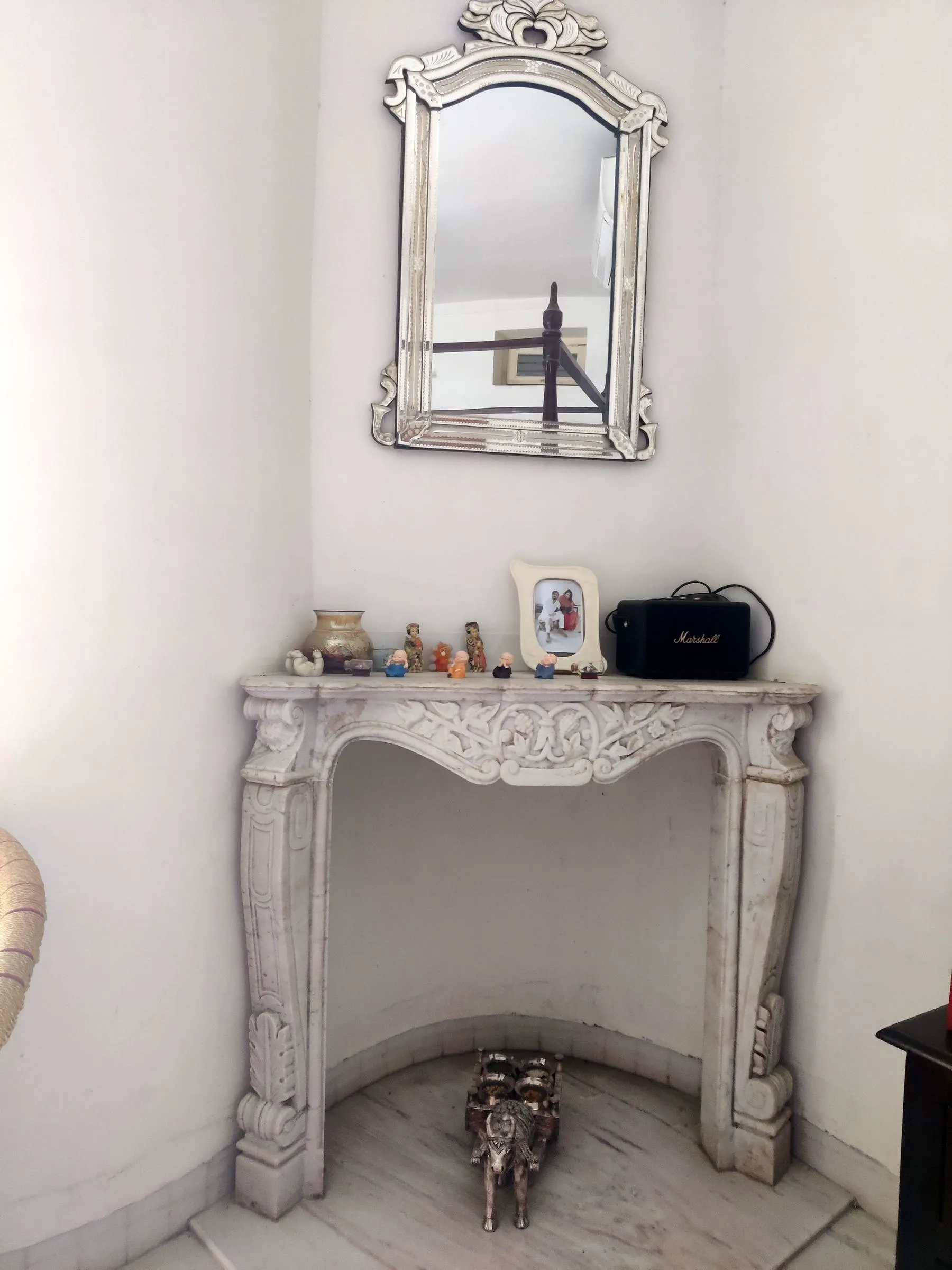 A carved white marble fireplace set into a corner of the house, an ornate mirror above it