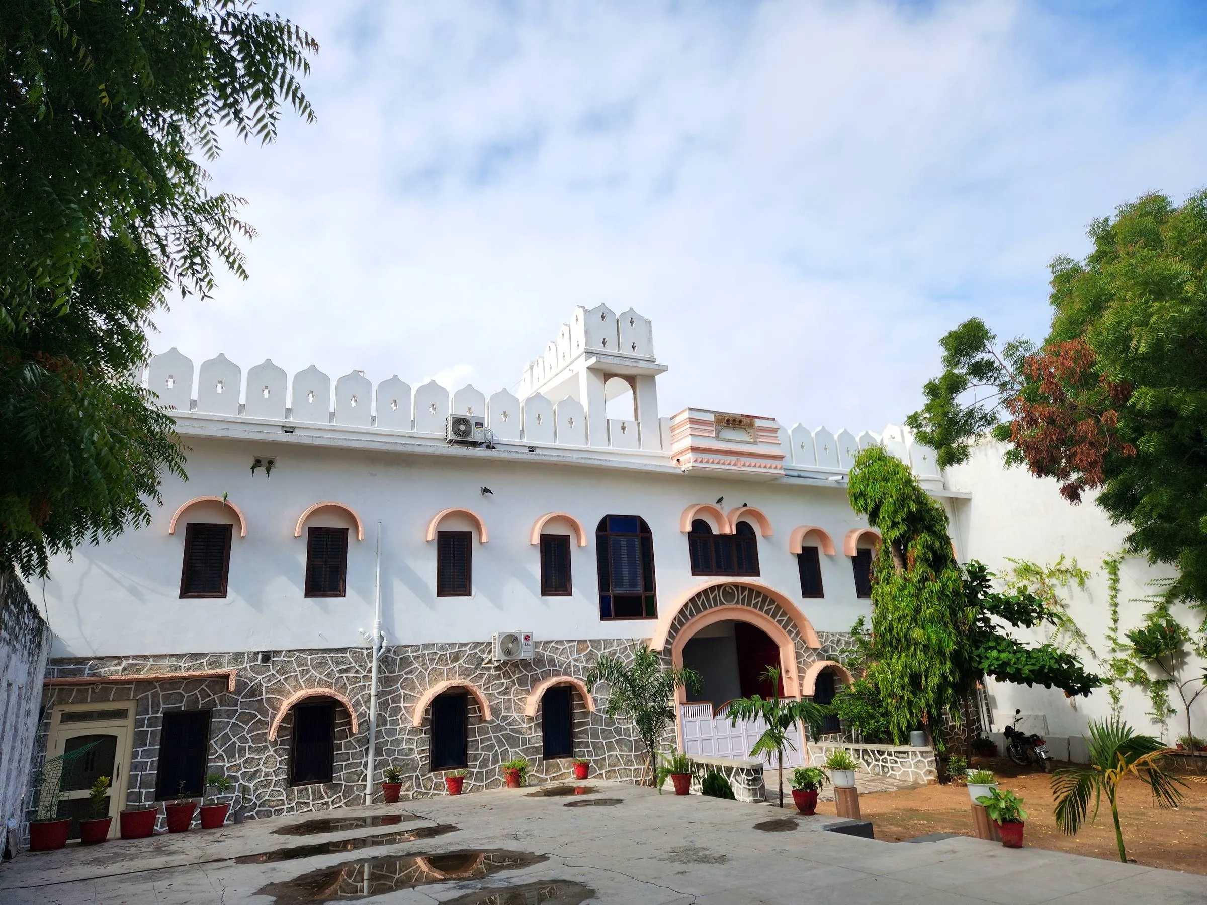 Rawla Bankli — the white heritage house behind its courtyard, crenellated parapet and pink-trimmed arches framed by old trees