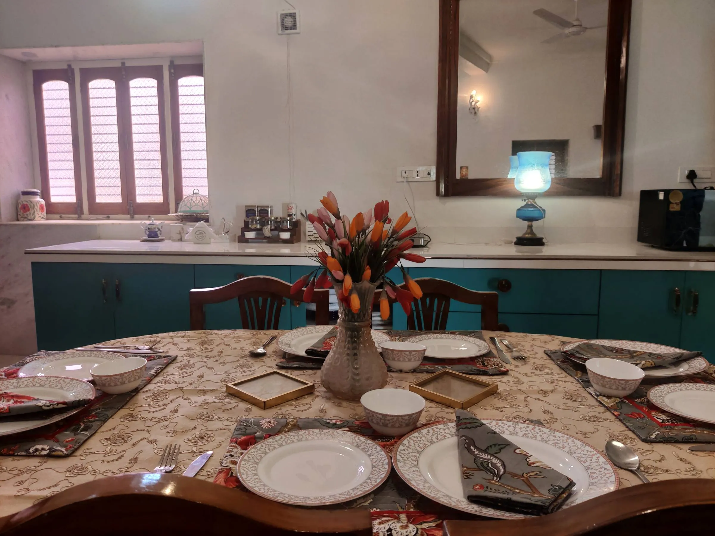 The dining table at Rawla Bankli laid for a meal — patterned mats, white china and a vase of tulips, the kitchen behind